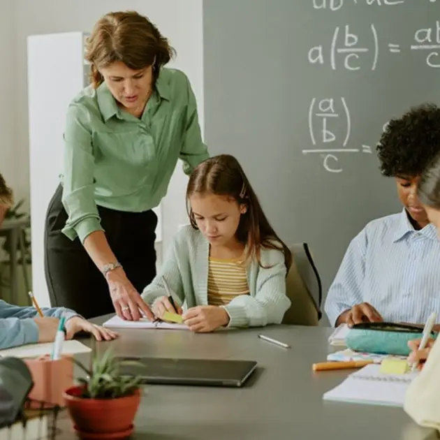 Teacher helping students at chalkboard with math equations